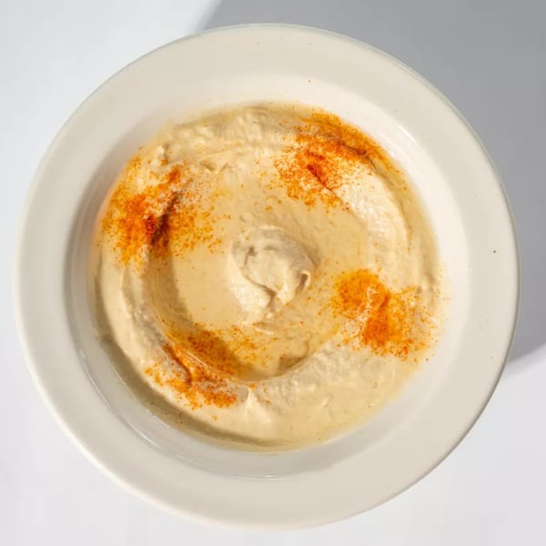 Creamy hummus in a white bowl, garnished with a swirl of paprika.