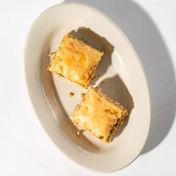 Two pieces of baklava with a golden-brown top and pistachio filling on an off-white oval plate.