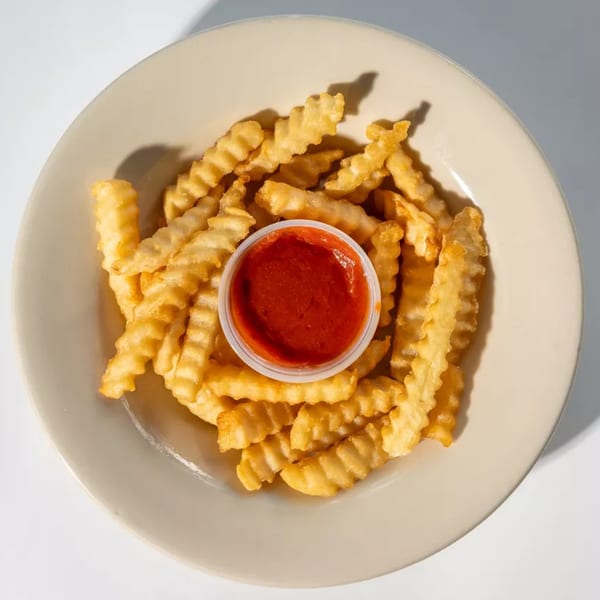 A plate of golden crinkle-cut fries with a small cup of red ketchup in the center.