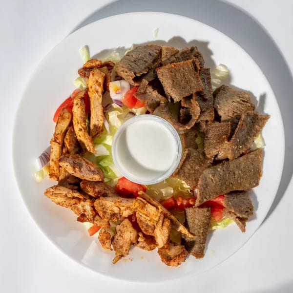 Chicken and gyro meat over lettuce, tomatoes, and onions with a side of white sauce.