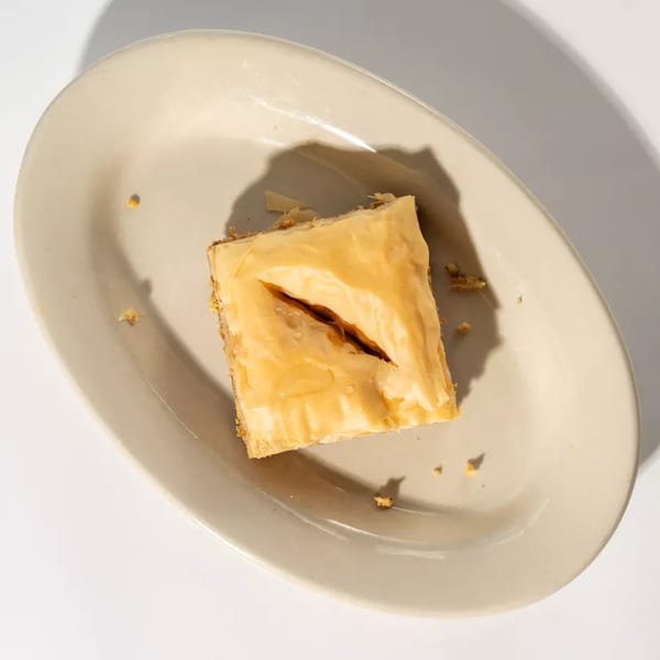 A square piece of baklava with a cut in the middle, drizzled with syrup, on a light plate.