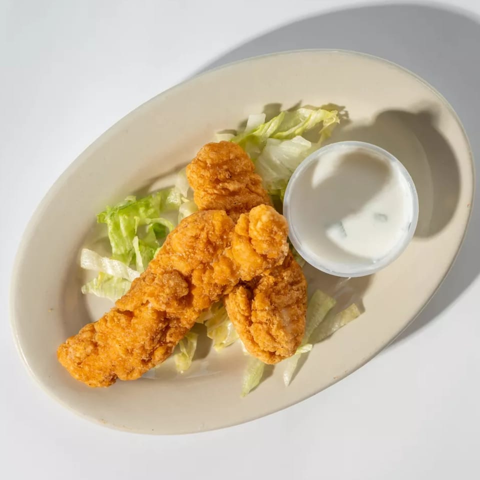 Three crispy chicken tenders on a bed of lettuce with a side of dipping sauce.